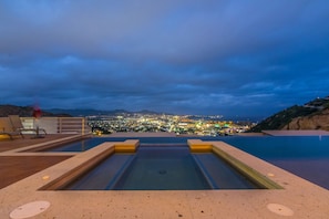 Piscina infinita no terraço com vista para a cidade ao entardecer.