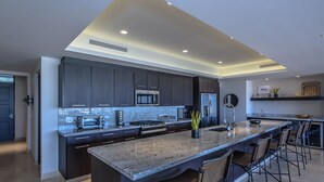 Una cocina moderna con armarios oscuros, una isla grande con taburetes de bar e iluminación empotrada en el techo.