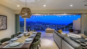 Un área de comedor con vista a un paisaje urbano al anochecer, una lámpara colgante moderna y una chimenea.