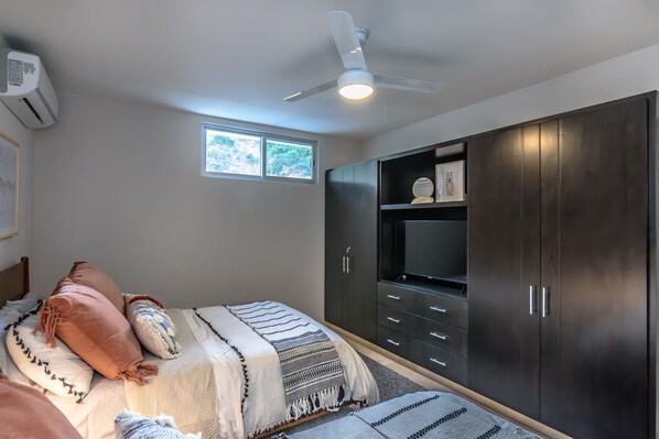 Un dormitorio con cama, ventilador de techo, ventana y armario oscuro.