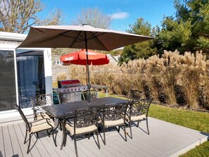 Eine Terrassenanlage im Freien mit Tisch, Stühlen, einem roten Sonnenschirm und einem Grill.