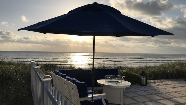 A patio with outdoor seating, a table, and an umbrella overlooking the ocean. - 4 Bdrm/3 Bath The Tatum House Cottage - Direct Oceanfront (New Smyrna Beach)