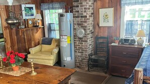 Interior rústico de cabana com mesa de jantar de madeira, um sofá, um frigorífico e uma parede de tijolos.
