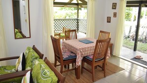 A dining area with a table, chairs, and a view of the outdoors. - Rona Kaitangata - across the road from the beach (Muri Beach)