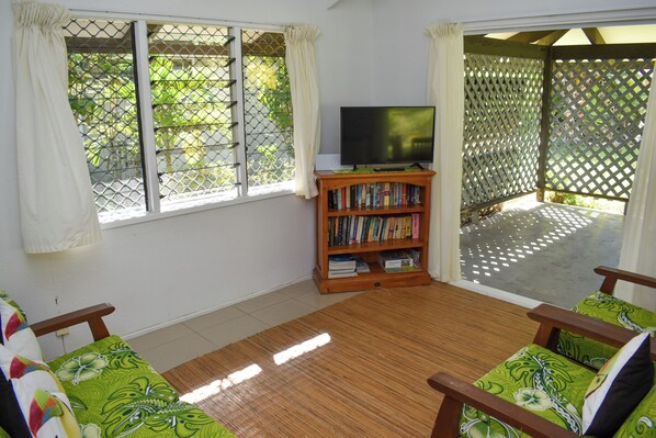 A room with a wooden floor, a television on a stand, a bookshelf, and two green patterned chairs.