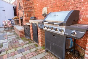 Ein gemauerter Grill mit Schornstein, ein Mülleimer und eine Grillabdeckung.