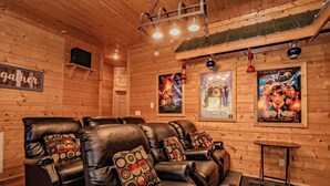 A cozy room with wooden walls and ceiling, featuring leather recliners with patterned cushions, a small table, and movie posters on the wall. - SmokyMountainHigh: Pets, Hot Tub, Wifi, Resort Pool, Theater, Games, Fire Pit (Pigeon Forge)
