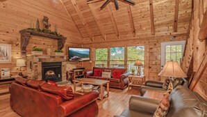 A cozy log cabin interior with a fireplace, leather sofas, and a television. - SmokyMountainHigh: Pets, Hot Tub, Wifi, Resort Pool, Theater, Games, Fire Pit (Pigeon Forge)