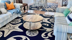 A spacious living room with a ceiling fan, a dining area with white chairs, and a large patterned rug. - Cape May Vacation Rentals-1 block to beach & 2  to town! Walk everywhere! (Cape May)
