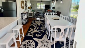 A spacious kitchen with white cabinetry, a large island, and a dining area with white chairs and a star-patterned rug. - Cape May Vacation Rentals-1 block to beach & 2  to town! Walk everywhere! (Cape May)