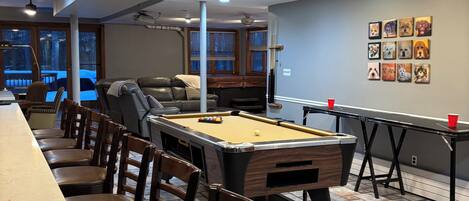 A pool table with chairs, a bar area, and a wall with framed pictures.