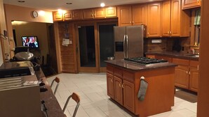 A modern kitchen with wooden cabinets, a stainless steel refrigerator, a gas stove, and a dining area with a table and chairs.