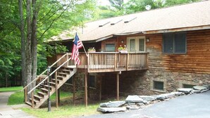 A wooden cabin with a stone foundation, a wooden deck, and a staircase leading to a porch.