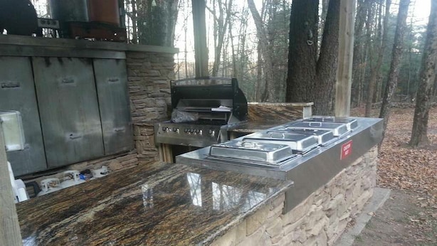 An outdoor kitchen with a stone wall, a gas stove, and a grill.