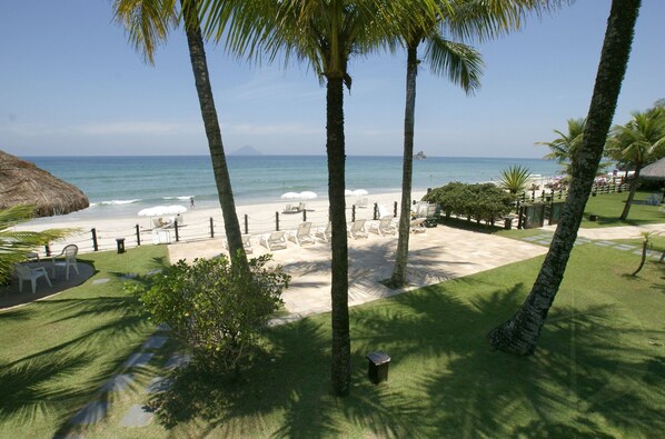 A beach view with palm trees, a thatched-roof structure, and beach chairs.