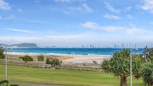 Küstensicht mit Strand, einer Rasenfläche und einer entfernten Stadtlandschaft.
