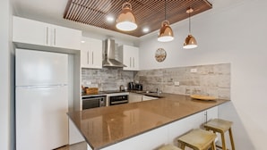 Eine moderne Küche mit weißen Schränken, einer Granit-Arbeitsplatte, einem Edelstahl-Kühlschrank, einer Kaffeemaschine und einer Uhr an der Wand.
