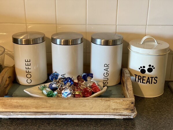 En köksbÀnk med tre vita förvaringsbehÄllare mÀrkta med "Kaffe", "Socker" och "Gott", samt en trÀbricka med ett urval av choklad.