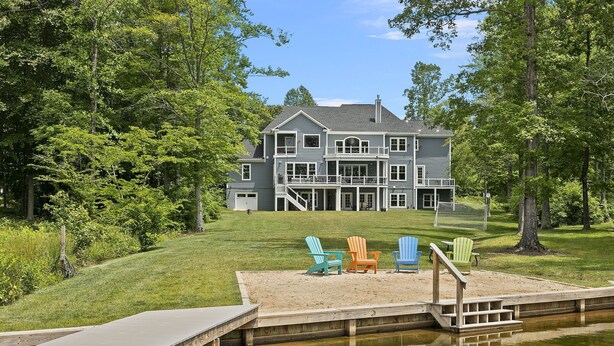 A large house with a dock extending into a pond, surrounded by lush greenery. - Luxury Lakefront Estate on Lake Anna 8,000 SqFt, Private Beach & Dock, Sleeps 20 (Bumpass)