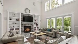 A spacious living room with a fireplace, comfortable seating, and large windows offering a view of the outdoors. - Luxury Lakefront Estate on Lake Anna 8,000 SqFt, Private Beach & Dock, Sleeps 20 (Bumpass)