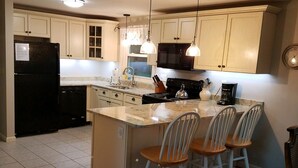 A kitchen with a central island, white bar stools, a black refrigerator, and a stove. - Charming Classic Cape Home Bordering Bike Trail-Family Friendly In Harwich (Harwich)
