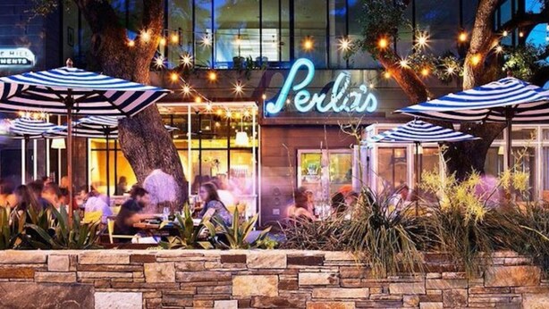 Un ristorante chiamato 'Perla's' con posti a sedere all'aperto e ombrelloni a righe.