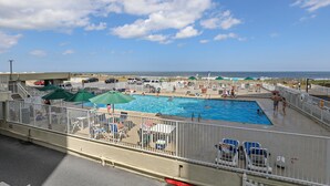 A rooftop pool with a view of the ocean, surrounded by lounge chairs and umbrellas.