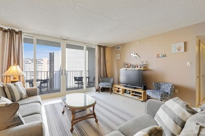 A living room with a sofa, armchairs, a TV, and a balcony with a view of buildings.