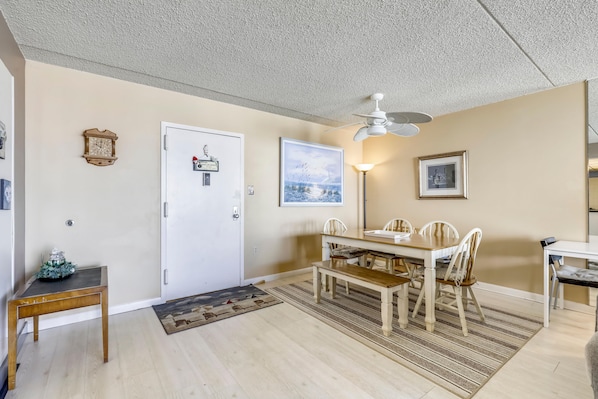 A dining area with a white table, chairs, and a bench. There is a ceiling fan, a clock, and a door with a sign. - FREE DAILY ACTIVITIES & LINENS INCLUDED*! 2bed/2bath Quayh condo available for a mini-week! (Ocean City)