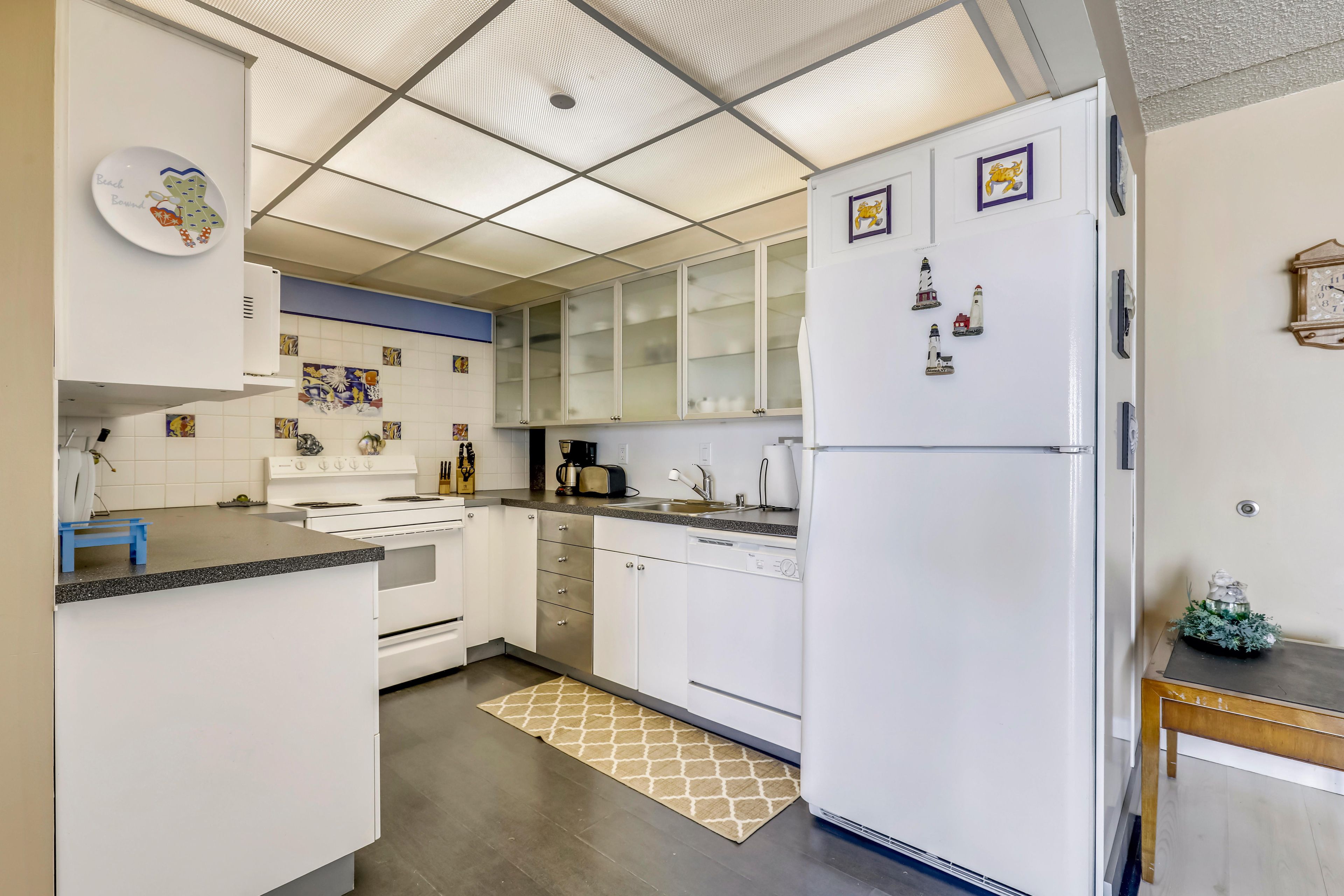 Una cocina moderna con armarios blancos, horno empotrado, refrigerador y cafetera.
