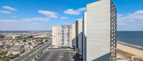 Een hoog gebouw met een parkeerplaats ervoor, met uitzicht op een strand.