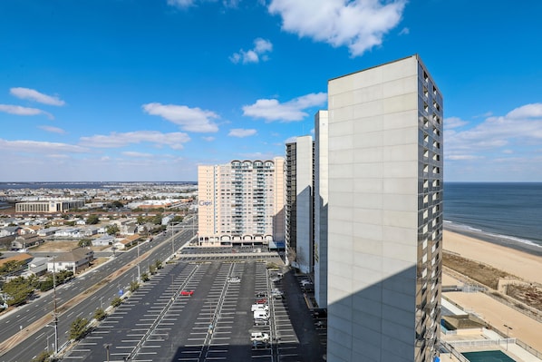 A high-rise building with a parking lot in front, overlooking a beach.