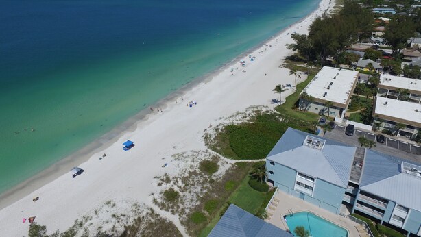 An aerial view of a beach with a swimming pool and a building with a flat roof. - 1 Block to Beach on Private Lake Heated Pool, SPA  6937 Holmes Blvd. (Holmes Beach)