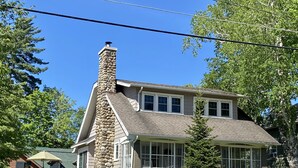 Une maison à deux étages avec une cheminée en pierre, une clôture en bois peinte en blanc et une pelouse bien entretenue.
