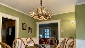 Une salle à manger avec une table à plateau de verre entourée de chaises en bois, un lustre et des tableaux encadrés accrochés aux murs.