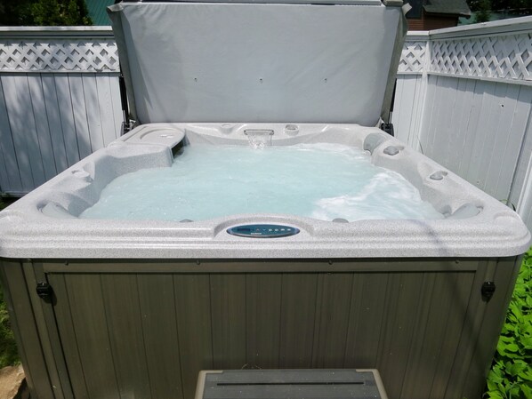 A hot tub with a control panel, surrounded by a wooden fence.