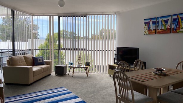 Een woonkamer met een bank, televisie, eettafel, stoelen en een gestreept vloerkleed.