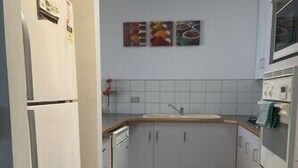 Een smalle keuken met witte kastjes, een koelkast, een magnetron en een spoelbak.