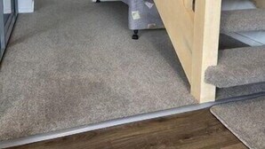 Een trap met een houten leuning die leidt naar een kamer met een vloerbedekking en een bank.