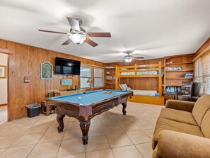 Une salle de jeux avec une table de billard, des ventilateurs de plafond, des lits superposés et un téléviseur.
