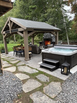Un bain à remous avec des marches, un foyer en pierre et du mobilier d’extérieur placé sous une pergola en bois.