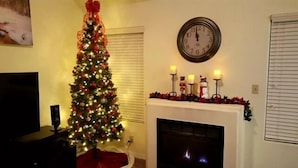 Un salon avec un sapin de Noël, une cheminée et une horloge au mur.