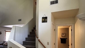 Un escalier avec une rampe, un interrupteur et une porte donnant sur une autre pièce.
