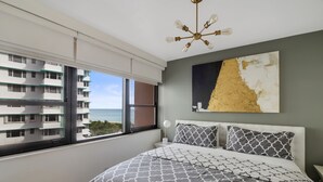 A bedroom with a large bed, a view of the sea through a window, and a ceiling light fixture. - Direct Ocean Front Property (Miami Beach)
