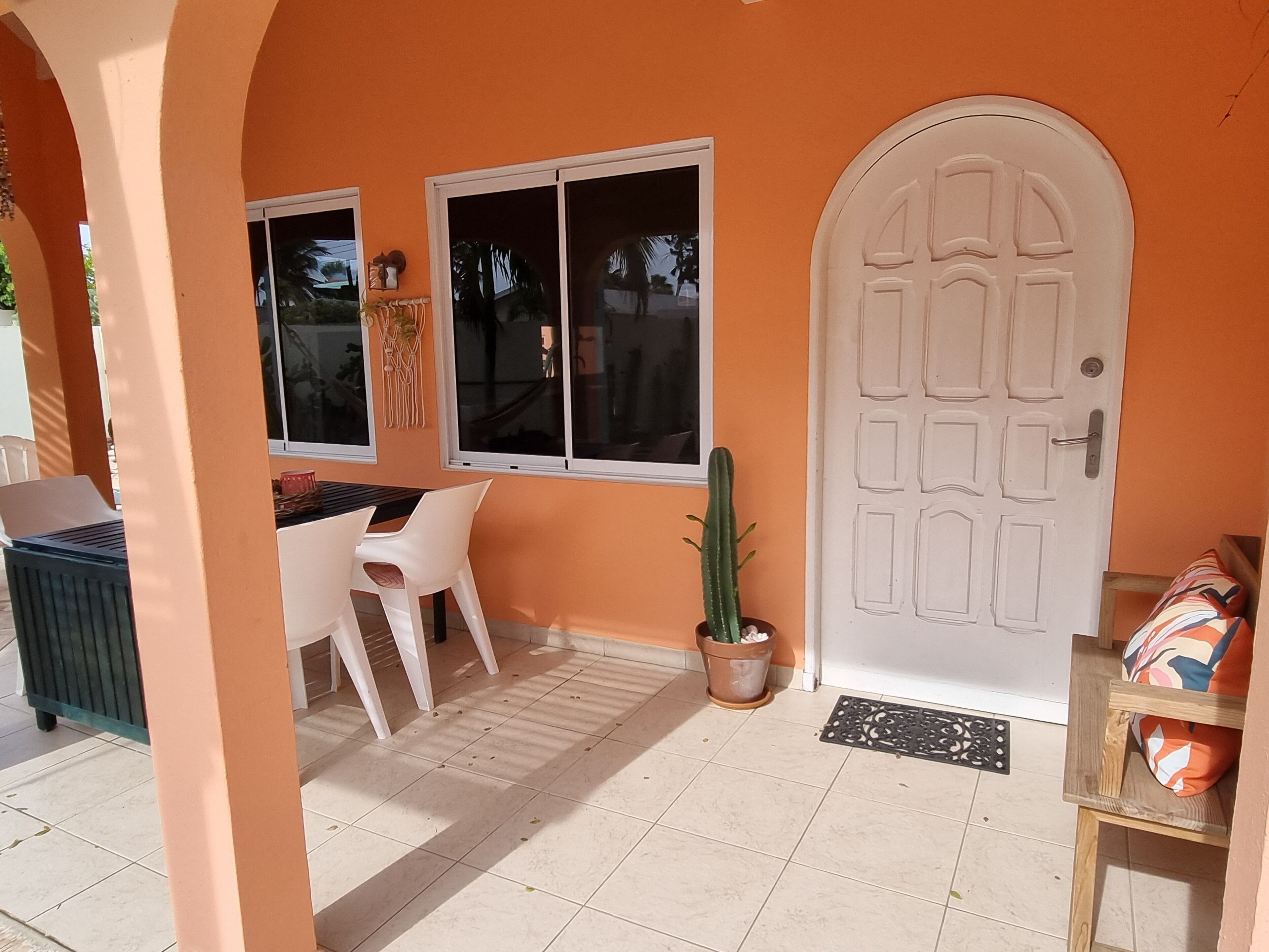 Una habitación con puerta blanca, ventana, un cactus y una mesa con sillas.