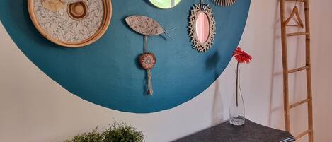 A room with a teal accent wall, a black desk with two patterned vases, a mirror, and a hanging decorative item.