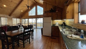 A spacious kitchen with wooden cabinets, a dining area with a table and chairs, and large windows offering a view of the outdoors. - Beautiful and roomy two bed, two bath cabin nestled in the Kiamichi Mountains (Hodgen)