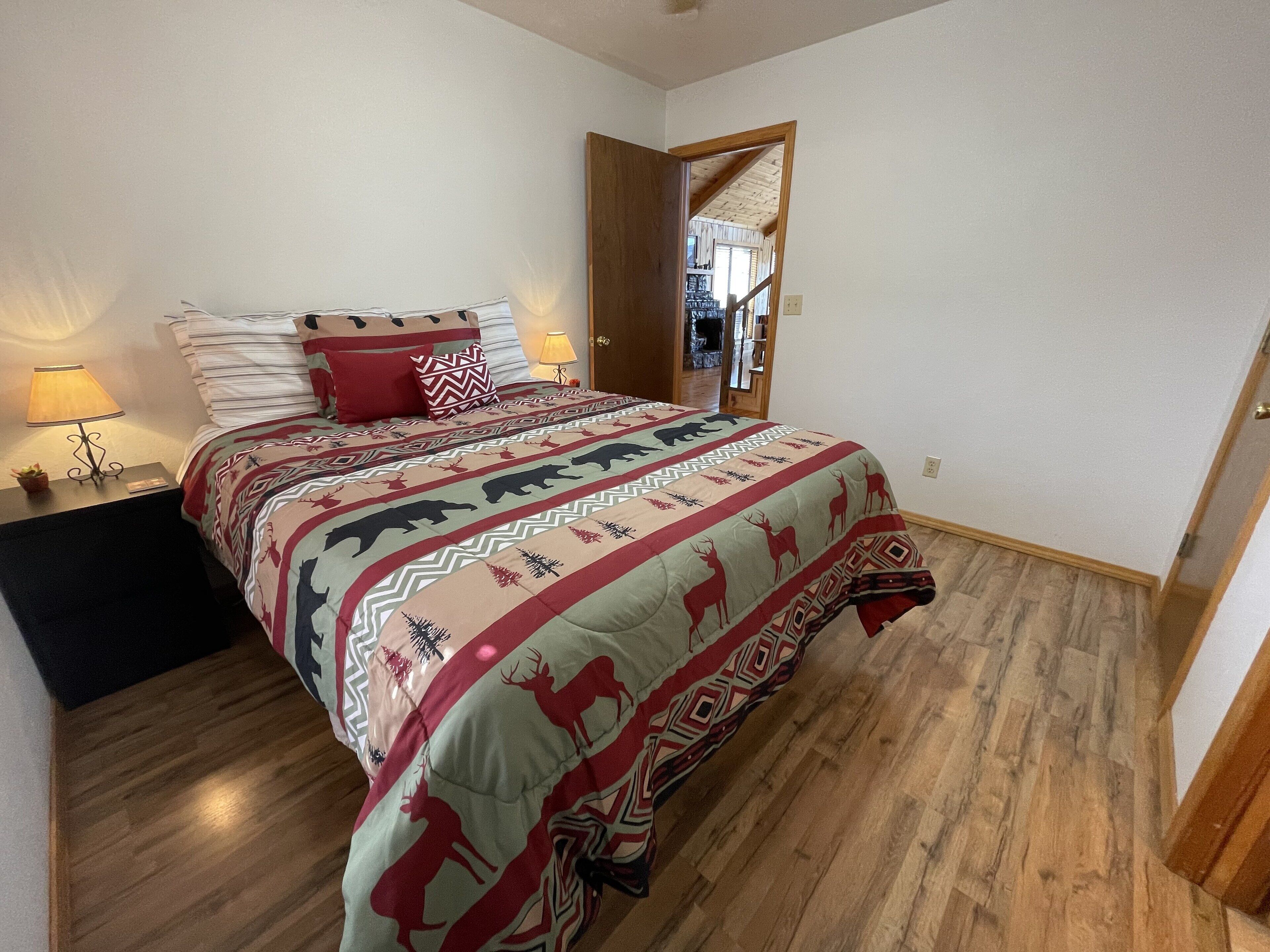 A bedroom with a bed, a nightstand, a lamp, and a door leading to another room.