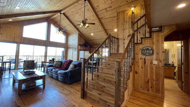 A spacious cabin interior with a wooden floor, a sofa, a dining table, and a staircase. - Beautiful and roomy two bed, two bath cabin nestled in the Kiamichi Mountains (Hodgen)