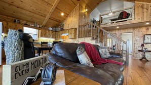 A cabin interior with a wooden interior, a leather couch, a sign reading "CLIMB EVERY MOUNTAIN", and a staircase leading to an upper level. - Beautiful and roomy two bed, two bath cabin nestled in the Kiamichi Mountains (Hodgen)